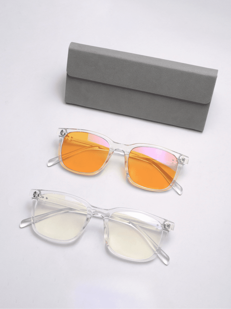 Zwei transparente Brillen mit klarem Gestell, eine mit orangefarbenen Spiegelgläsern und eine mit leicht gelben Gläsern, daneben ein graues Etui