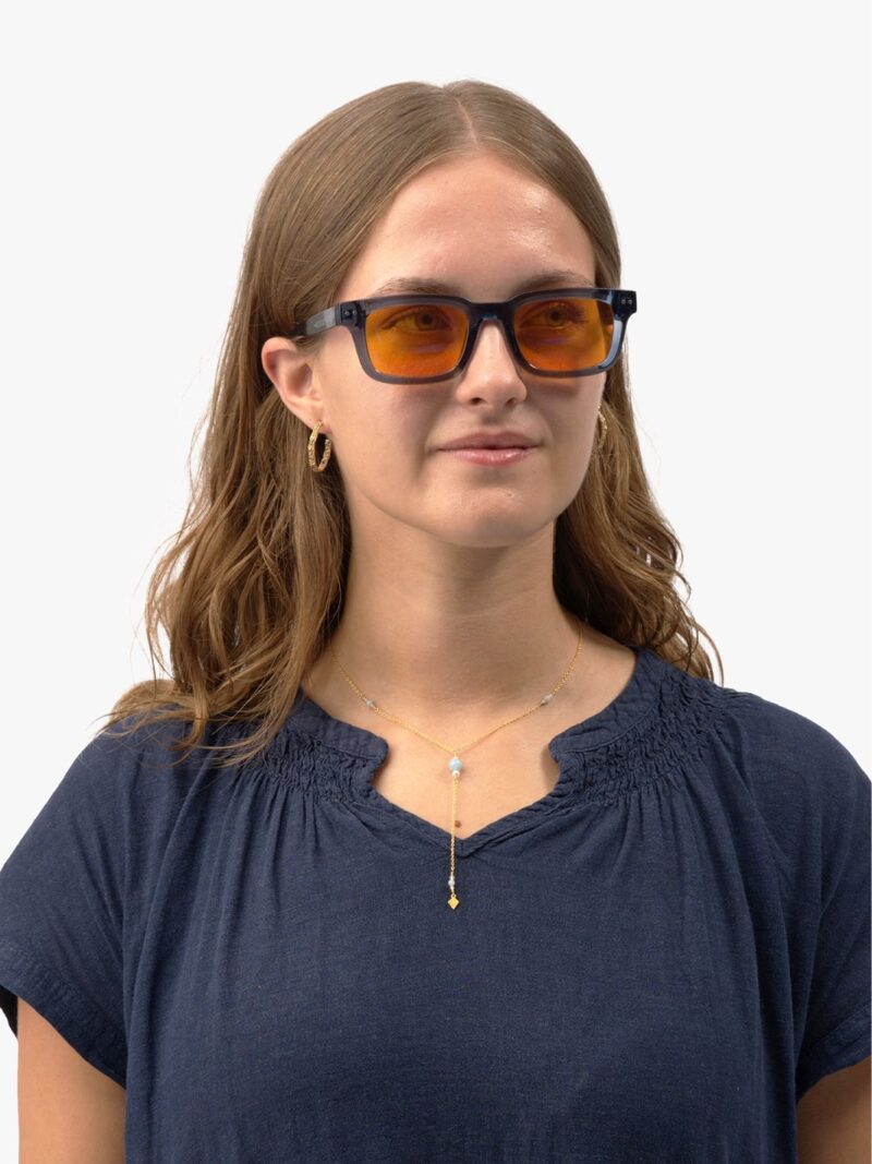 Frau mit der blauen rechteckigen Eclipse 90 Brille mit orangefarbenen Gläsern, goldenen Ohrringen und blauer Bluse