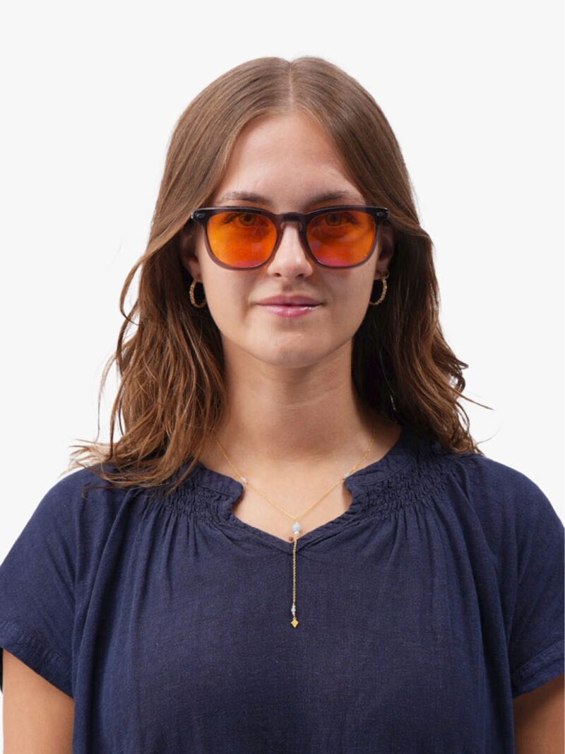 Junge Frau mit orangefarbener Sonnenbrille, dunkelblauer Bluse, goldenen Creolen und feiner Goldkette
