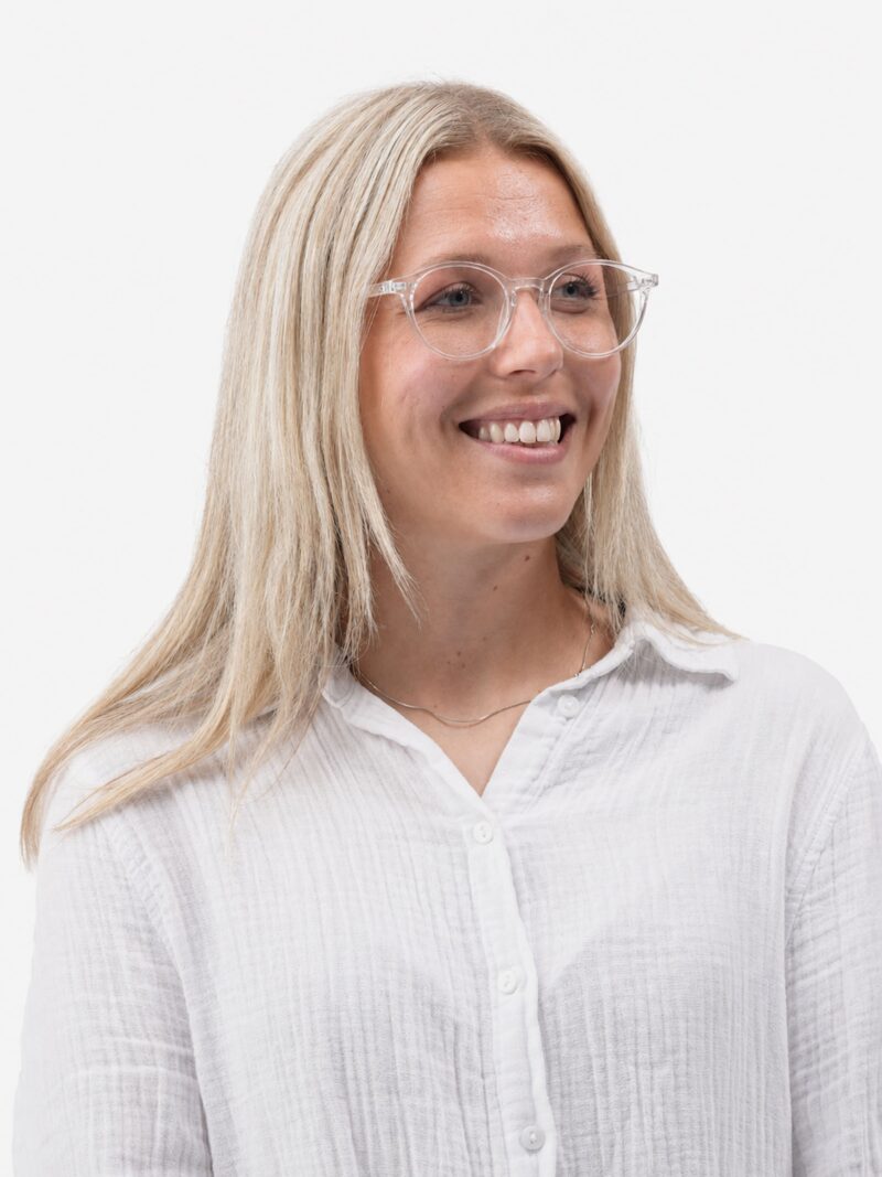 Lächelnde Frau mit blonden Haaren, transparentem Brillengestell und weißer Bluse