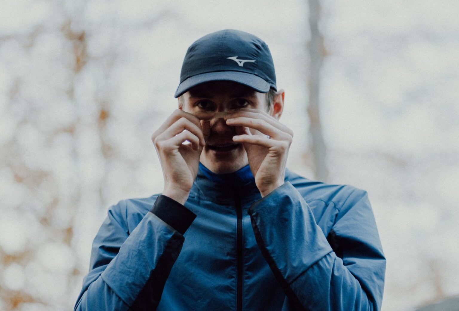 Mann in blauer Laufjacke und Cap bringt vor dem Lauf einen Nasenstrip an