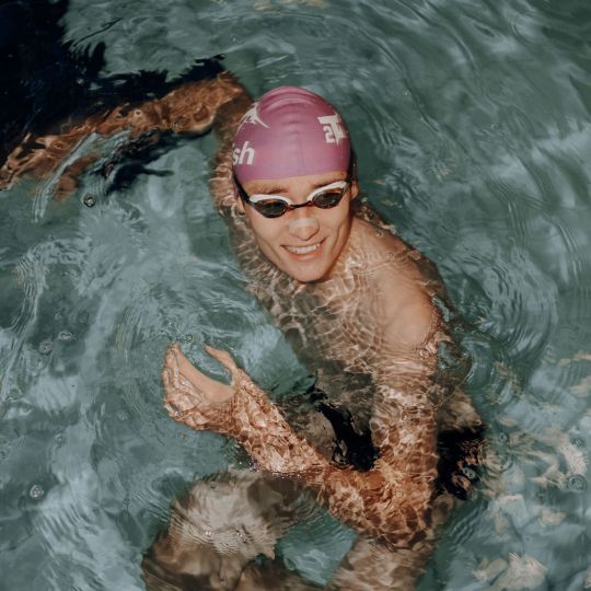 Lächelnder Schwimmer mit rosa Badekappe und Schwimmbrille im Wasser