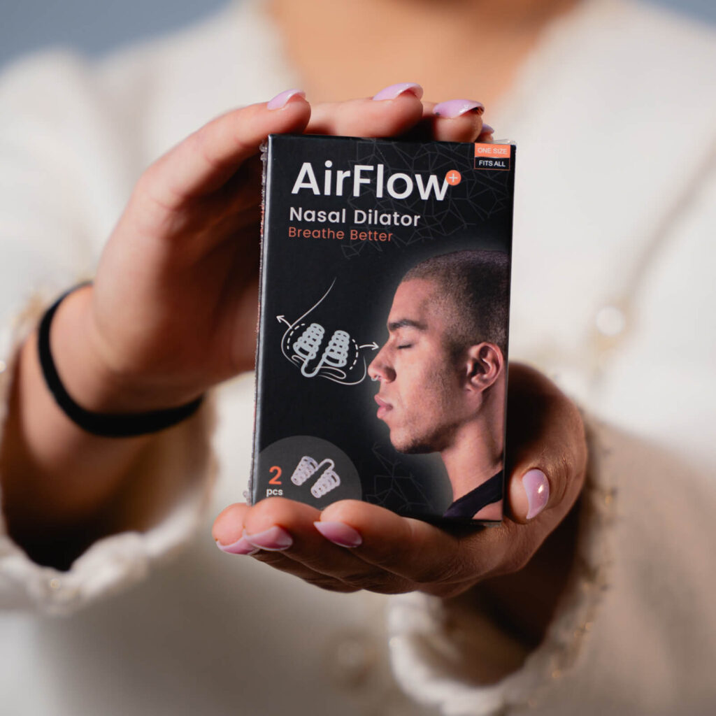 Hände mit rosafarbenem Nagellack halten Verpackung des AirFlow Nasal Dilator mit Profilporträt und Illustration