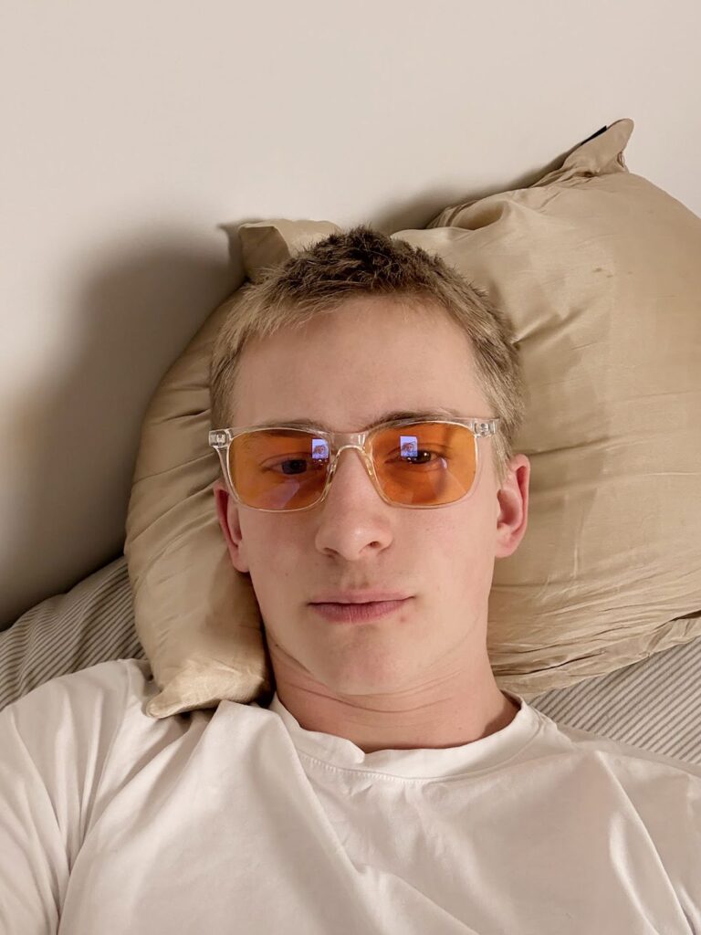 Junger Mann liegt auf Kissen und trägt klare Brille mit orangefarbenen Gläsern