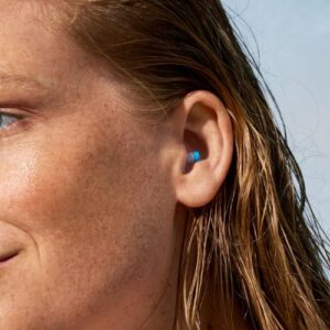 Seitliche Nahaufnahme einer Frau mit nassen Haaren und blauem Ohrstöpsel, leichtes Lächeln
